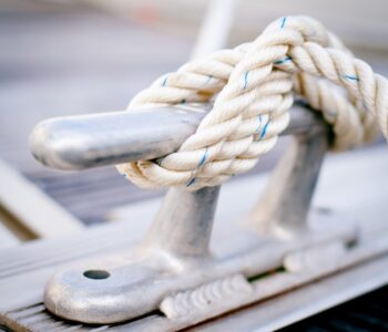 Closeup of white mooring rope tied around steel anchor on boat or ship.